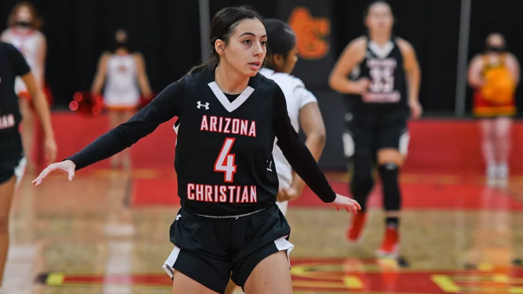 Female basketball player in black Arizona Christian jersey #4 on a gym court, extending arms as she moves.