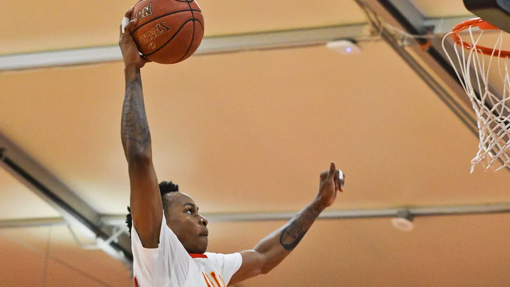 Basketball player in a white jersey dunks the ball with an extended arm toward the hoop in a gym.