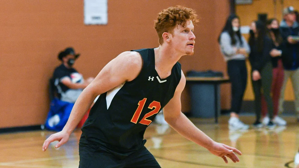 Male basketball player wearing a black jersey with number 12, dribbling on a gym court.
