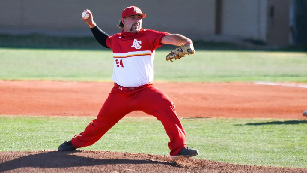 Baseball pitcher in red and white uniform on the mound delivering a pitch.