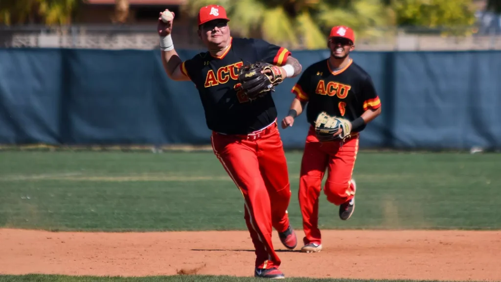 Two ACU baseball players in black and red uniforms sprint across the infield, with the foreground player raising his glove.