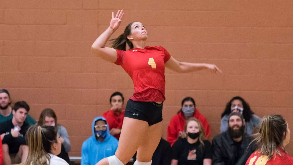 Female volleyball player in red jersey #4 leaps for a spike in an indoor gym as spectators watch from the stands.
