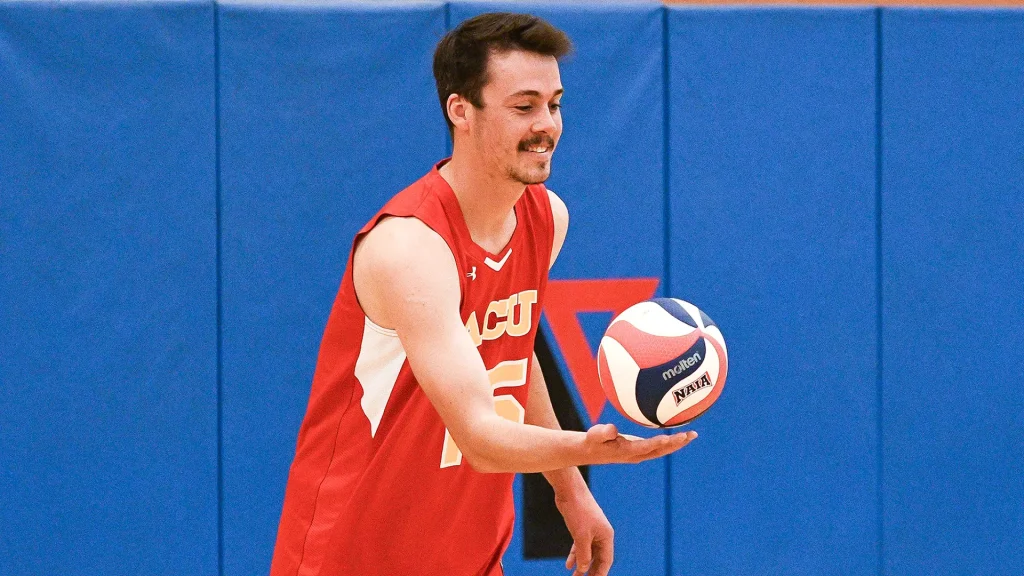 Male volleyball player in a red jersey passes the ball in a gym with blue padded walls