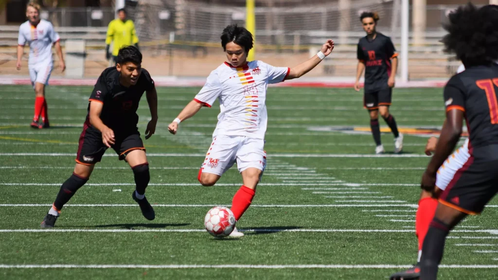 Soccer players in white and black uniforms contest the ball on a green turf field during a match.