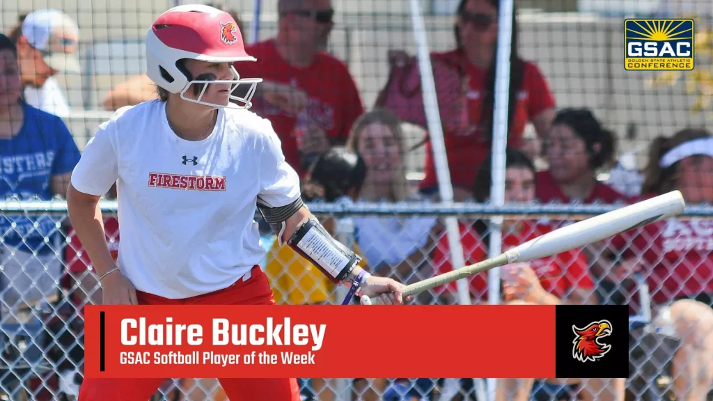 Female softball player in a white Firestorm shirt and red helmet swings a bat, with a cheering crowd behind a chain-link fence and a red banner reading “Claire Buckley – GSAC Softball Player of the Week.”