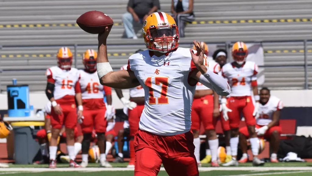 Quarterback in white and red jersey number 17 throws a pass during a football game, with teammates in red and white watching in the background.
