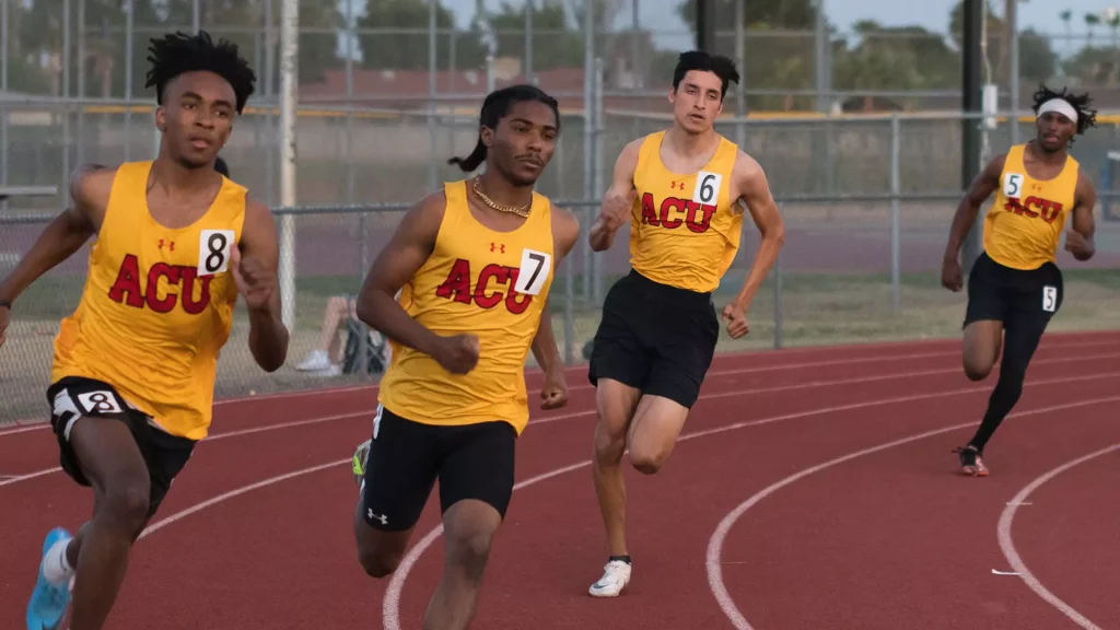 Four male sprinters in yellow ACU uniforms race on a red track, with bib numbers 8, 7, 6, and 5 visible.