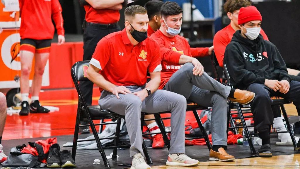 Basketball players sit on a bench during a game, wearing red jerseys and face masks.