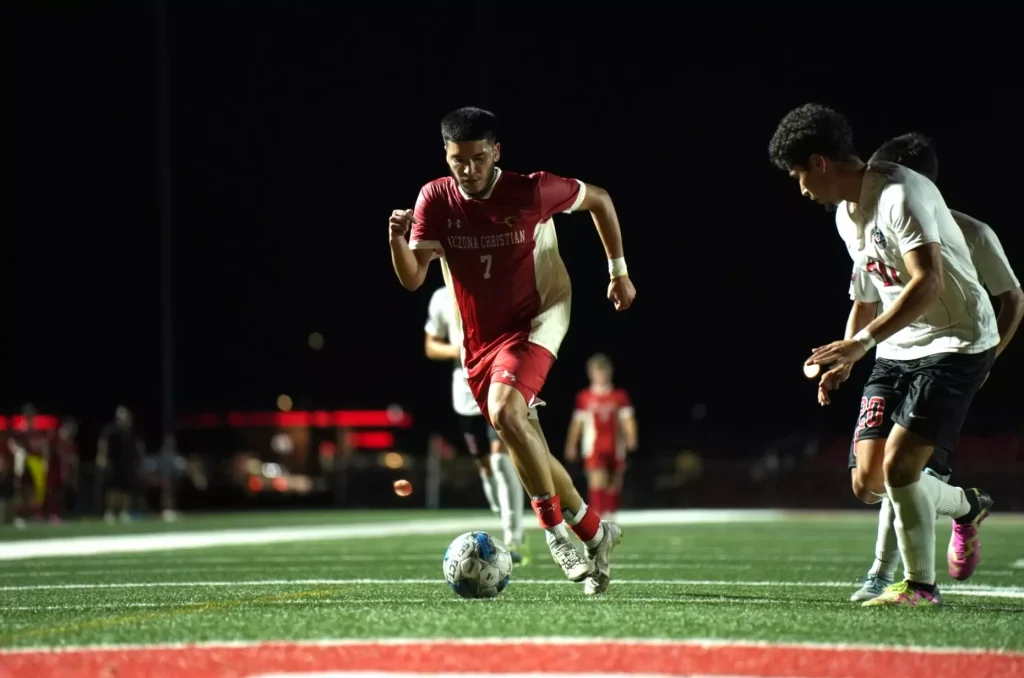 Soccer players sprint on a lit turf at night; a red jersey (#7) player controls the ball in foreground.