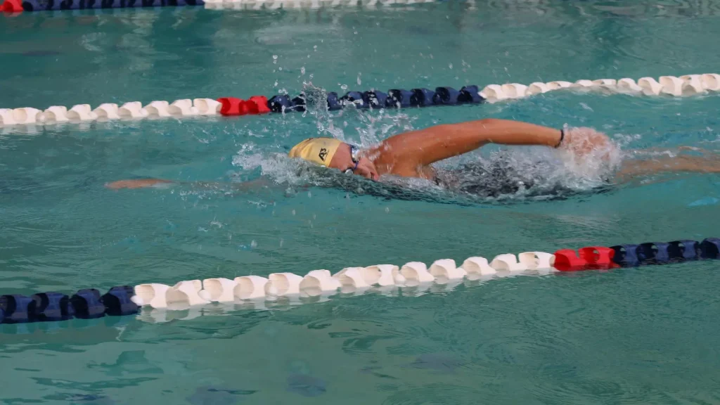 Swimmer in a yellow cap and goggles, performing freestyle in a pool lane with splash.