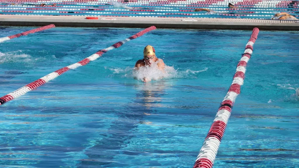 Swimmer in a yellow cap and goggles mid-stroke in a blue pool lane with red-and-white lane dividers.