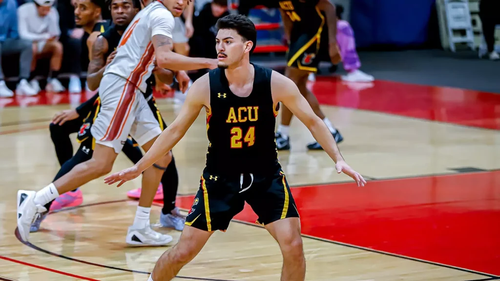 Basketball player in black ACU jersey #24 in a defensive stance on a crowded court during a game.