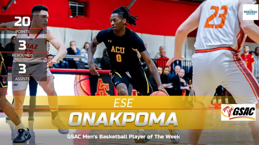 Basketball player in a black ACU jersey (number 0) dribbles past defenders during a GSAC game with spectators in the stands and a 'GSAC' logo visible on the court side.
