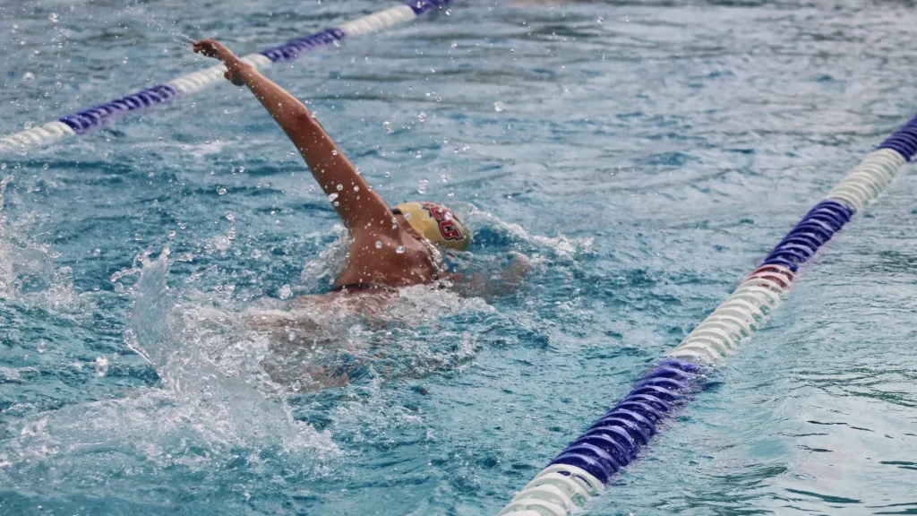 Swimmer in a lane performing a freestyle stroke, arm raised above the water with splashes around the pool.