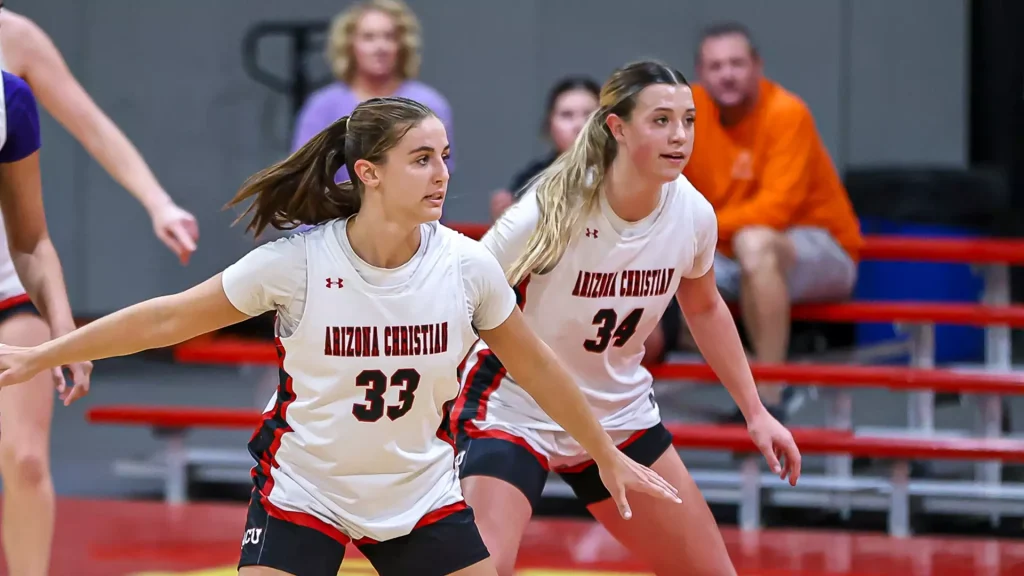Two Arizona Christian women’s basketball players in white jerseys (numbers 33 and 34) guard on the court during a game.