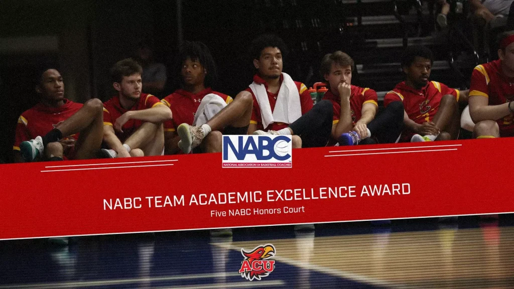 Basketball players in red uniforms sit on a bench behind a red NABC banner during an awards event; ACU logo visible below.