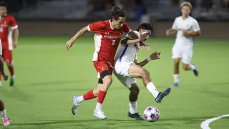 Soccer players in red and white chase the ball on a bright green field during a match.