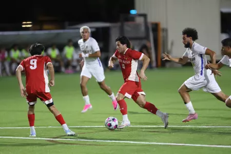 Soccer match at night: a red-team player dribbles the ball while white-team players chase on a green turf