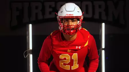 Football player in a red uniform with number 21 and a white helmet, standing in a lit entrance.