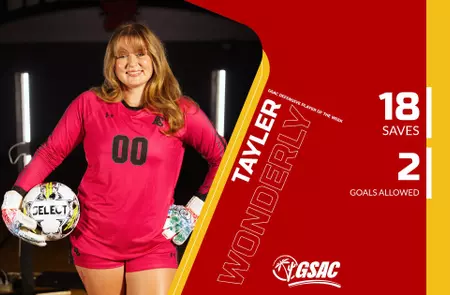 Female soccer goalkeeper in a pink uniform and gloves, holding a ball, standing in front of a red-yellow team graphic with a GSAC logo.
