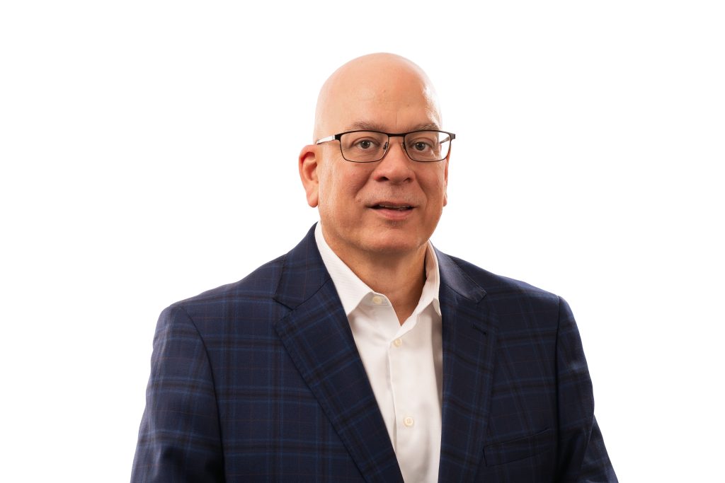 Portrait of a bald man wearing glasses and a blue plaid suit against a white background.