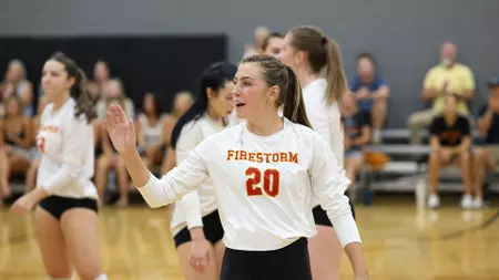 Female athlete in a white Firestorm jersey #20 gestures with her hand on a gym court during a game, teammates in the background.