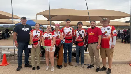 Group of ten people in red-and-white sports jerseys posing together under beige umbrellas at an outdoor event.