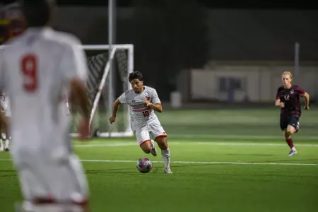 Soccer player in white controls the ball near the goal while defenders close in on a night game on a green field